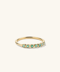 Bezel Emerald Half Eternity Band: 14k gold ring featuring bezel-set emerald gemstones, each unique with natural inclusions, showcased in a modern classic band design.