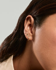 Close-up of an ear with Mini Heart Studs, featuring a tiny gold heart-shaped stud, a thin gold hoop, and a small round gold stud.