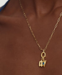 Person wearing an Oval Charm Enhancer gold necklace with a blue stone pendant, showcasing its elegant design and versatility for various styles.