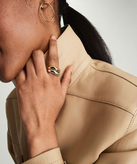 Close-up of Dôme Figure Ring Signature Bundle with polished gold and silver interlocking rings, worn on a hand with a beige leather jacket and gold hoop earring.