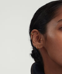 Close-up of a woman's ear wearing gold bar studs, highlighting the sleek and minimalist design of the earrings.