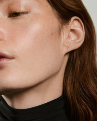 Close-up of an ear with a Piercing Studio - Baby Diamond Stud, a small, elegant gemstone earring nestled in the earlobe against freckled skin and reddish-brown hair.