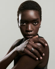 Young woman with short hair wears the Bold Open Dôme Ring, featuring an asymmetrical, open design, on her manicured hand, alongside small silver hoop earrings.