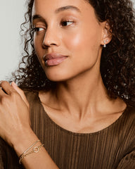 Young woman wearing Ada Double Pear Drop Earrings, featuring two pear-shaped gemstones. Earrings add shine and movement; complemented by gold bracelets on wrist.