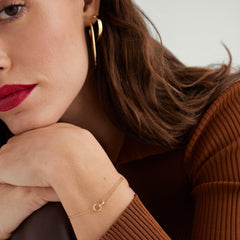 Linked Bracelet: A woman with her hand on her chin wearing a handcrafted 14k gold bracelet featuring two interlinked rings symbolizing strong personal bonds.