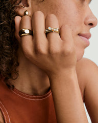 Close-up of a hand showcasing the Pavé Puzzle Stacking Ring, featuring architectural lines and pavé diamonds, alongside other gold rings and a simple stud earring.
