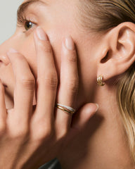 Close-up of a woman's face highlighting the Open Dôme Pavé Ring with interlocking gold bands, one plain and one diamond-set, on her manicured hand.