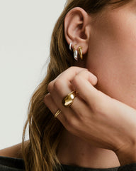 Jojo Double Hoops elegantly adorn a woman's ear, featuring a mixed metal design with an optical illusion, emphasizing fashionable jewelry style.