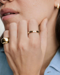 Hand showcasing Bold Dot Ring on middle finger, featuring small gold discs. Accompanied by a chunky gold band on the index finger.