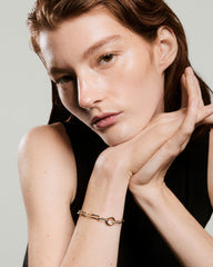 Young person wearing a sleeveless black top showcases the Paperclip Chain Charm Bracelet, featuring oval links and a circular ring detail on their wrist.