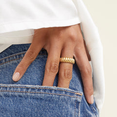 Hand wearing the Charlotte Ring, a gold accessory, partially tucked into the pocket of blue jeans.