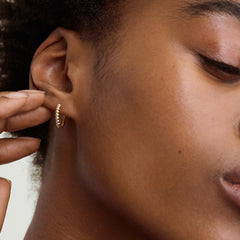 Close-up of a woman's ear wearing beaded small hoops, handcrafted in recycled 14k solid gold.