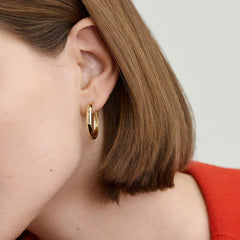 Close-up of a woman's ear adorned with bold, large handcrafted 14k recycled gold hoop earrings.