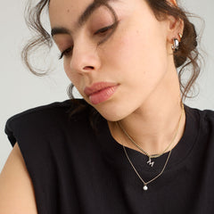 Woman wearing Mini Pearl Pendant Necklace, featuring a delicate chain and a single pearl, handcrafted in 18k gold vermeil, shown close-up with a black shirt.