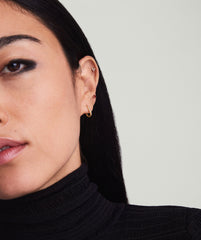 Close-up of a woman's ear wearing Gemstone Mini Studs: a tiny cluster stud on the helix, a red gem stud mid-ear, and a gold hoop on the lobe.