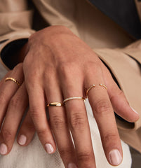 Close-up of a person's hands wearing the Diamonds Team Ring, showcasing its elegant design alongside other gold rings and a bracelet.