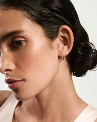 Profile view of a woman wearing Small Hoops, showcasing simple gold hoop earrings and a fine gold chain, highlighting their lightweight and everyday wear appeal.