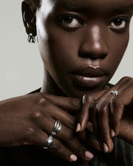 Dark-skinned person wearing the Bold Open Dôme Ring with sculptural silver design. Interlaced hands highlight the ring's open spaces and asymmetrical style.