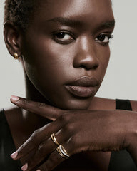 Black woman with gold hoop earring showcases Open Dôme Diamond Ring on raised hand, featuring sculptural design and trio of diamonds in 14k Salmon GoldTM.
