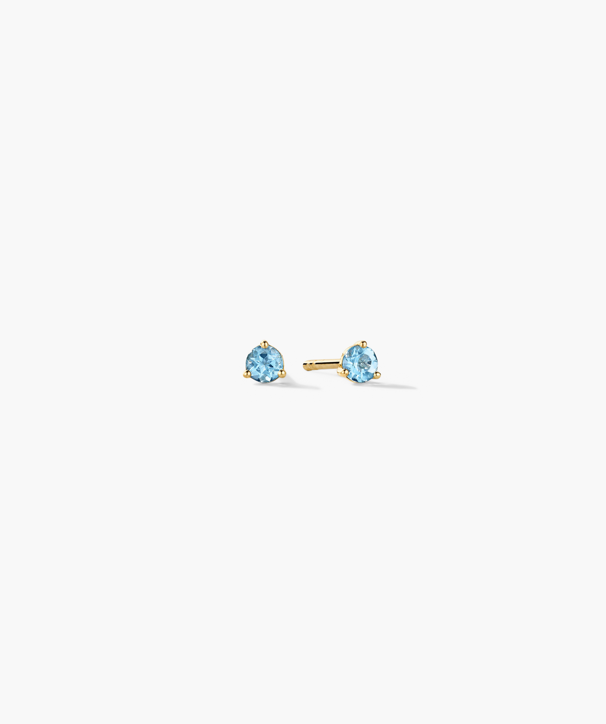 Gemstone Mini Studs featuring light-blue faceted gemstones in a three-prong yellow-gold setting, with a straight post and butterfly back, on a white background.