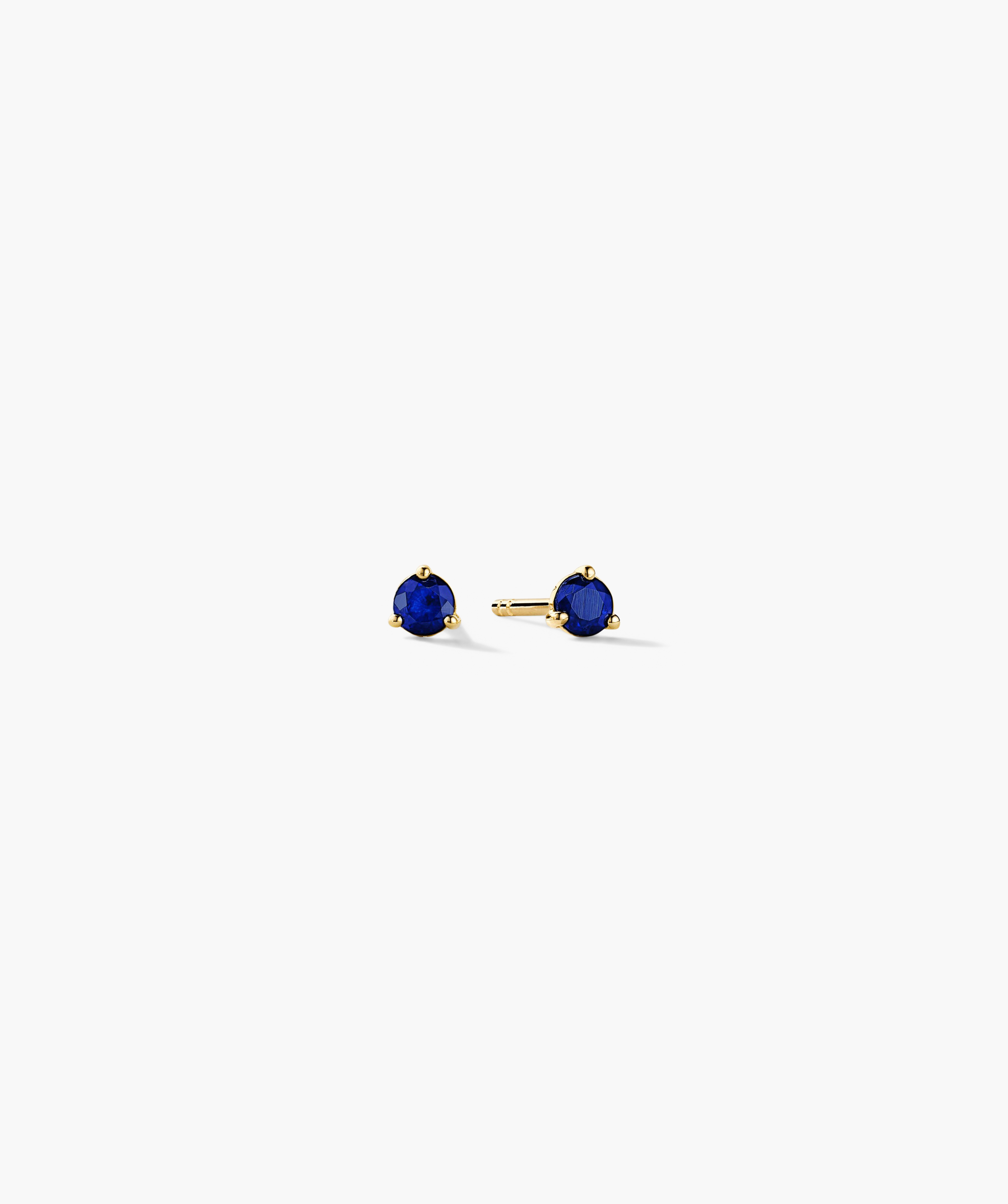 Gemstone Mini Studs featuring deep-blue gemstones in three-prong gold settings, showcasing one earring face-on and the other with a visible post and back.