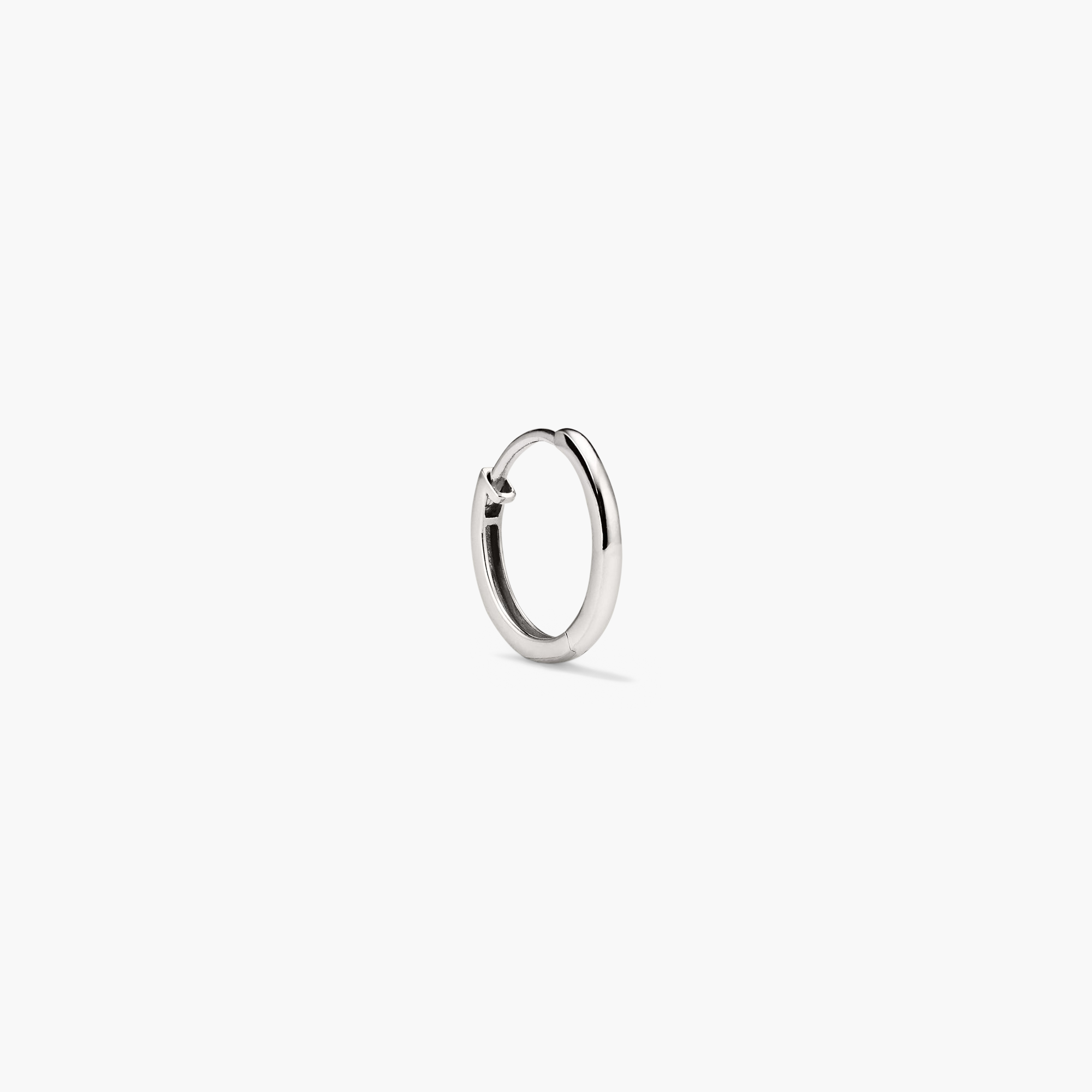 Single Easy Huggie Hoop: close-up of a silver hoop earring with a clicker closure, designed for everyday wear in handcrafted hollowed 14k gold.