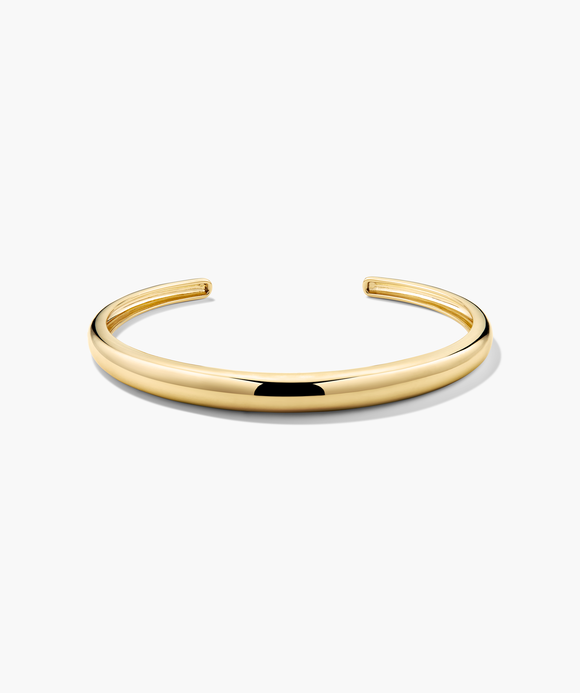 DÃ´me Cuff Bracelet: a polished gold-tone open-ended bangle, elegantly capturing a ray of sunshine, displayed on a simple white background.