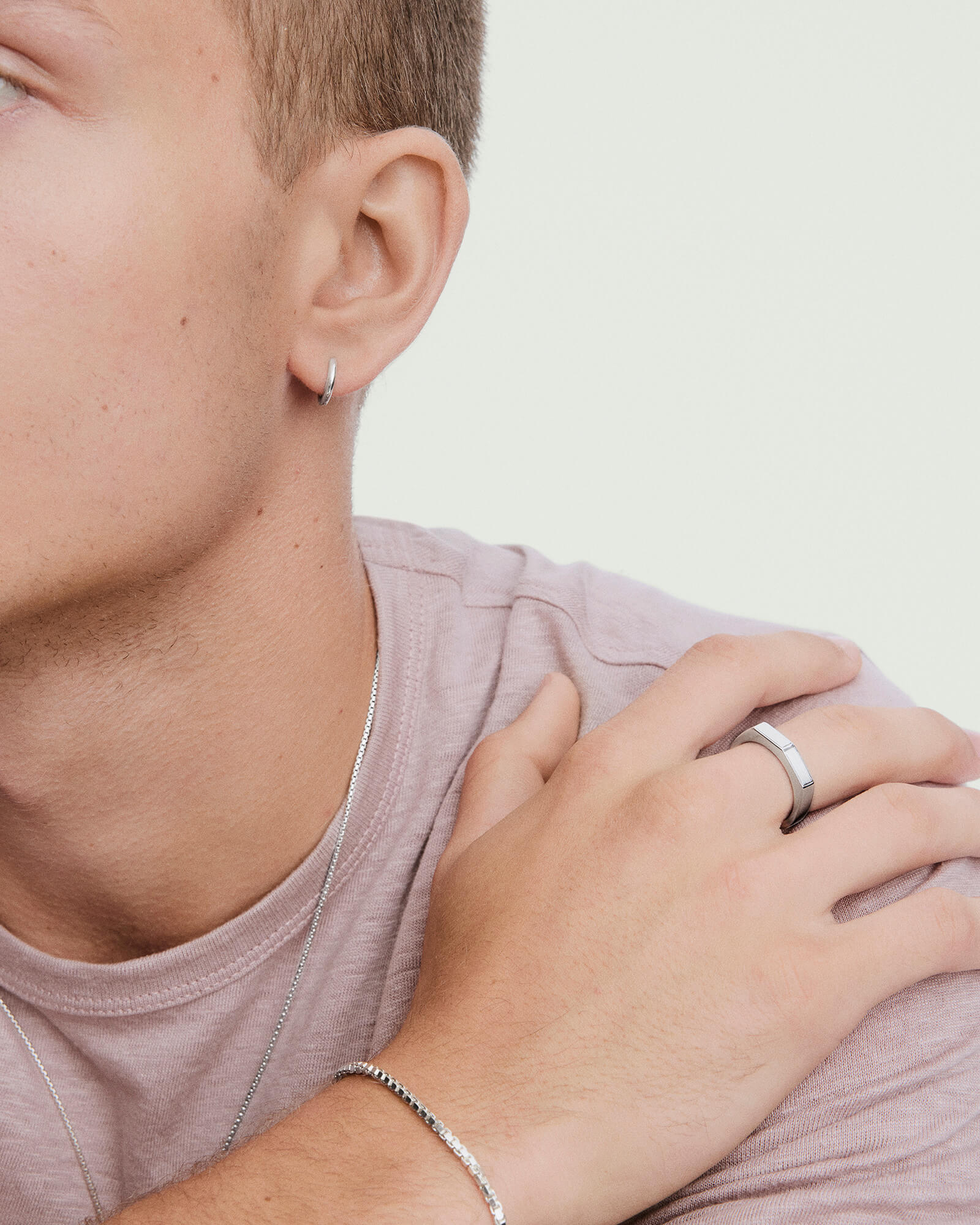 A young person showcases a Slim Faceted Ring on their index finger, complemented by other silver jewelry, including a hoop earring, chain necklace, and bracelet.