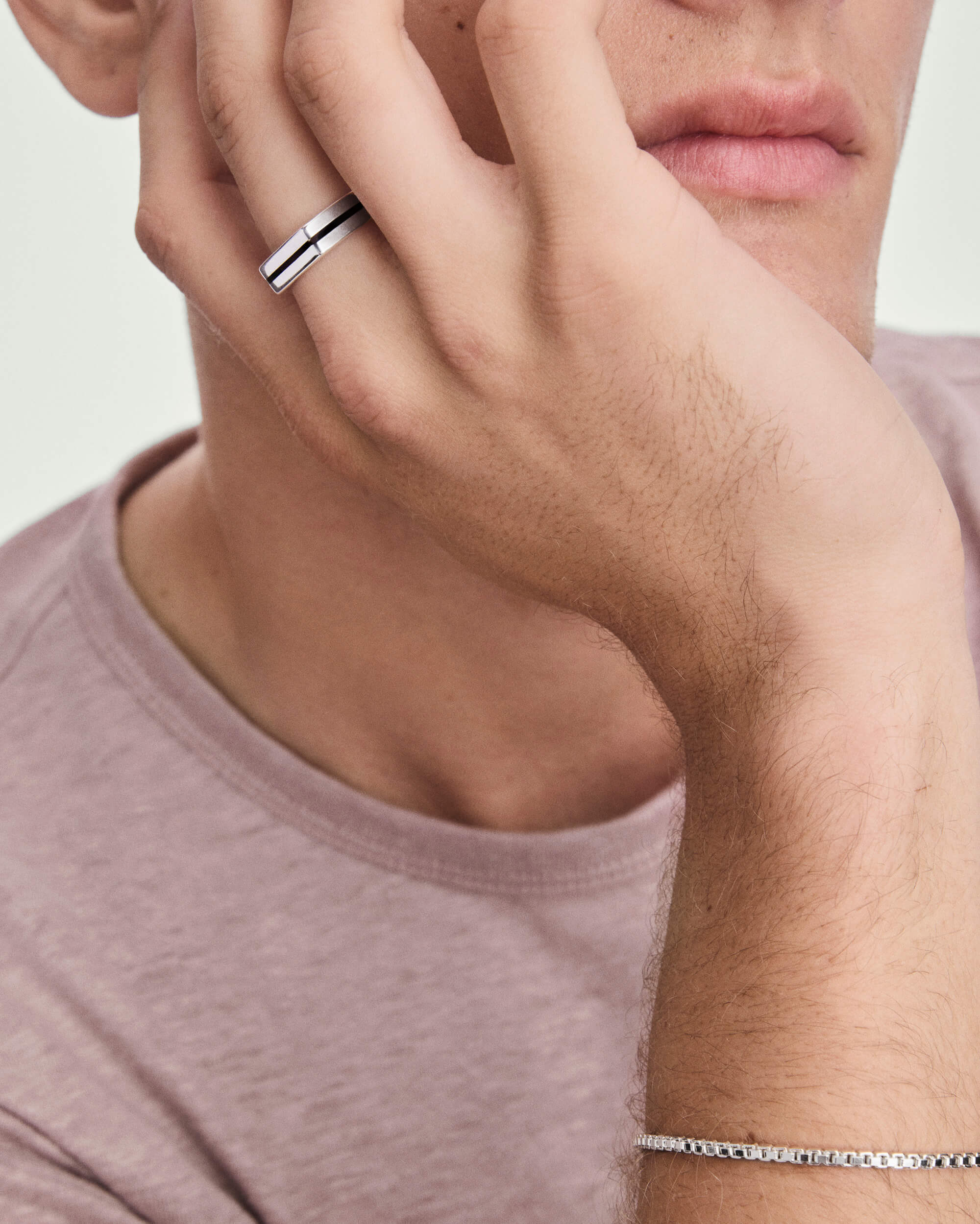 A young person wears a Slim Signet Ring with black enamel inlay on their middle finger, paired with a matching silver box-chain bracelet.