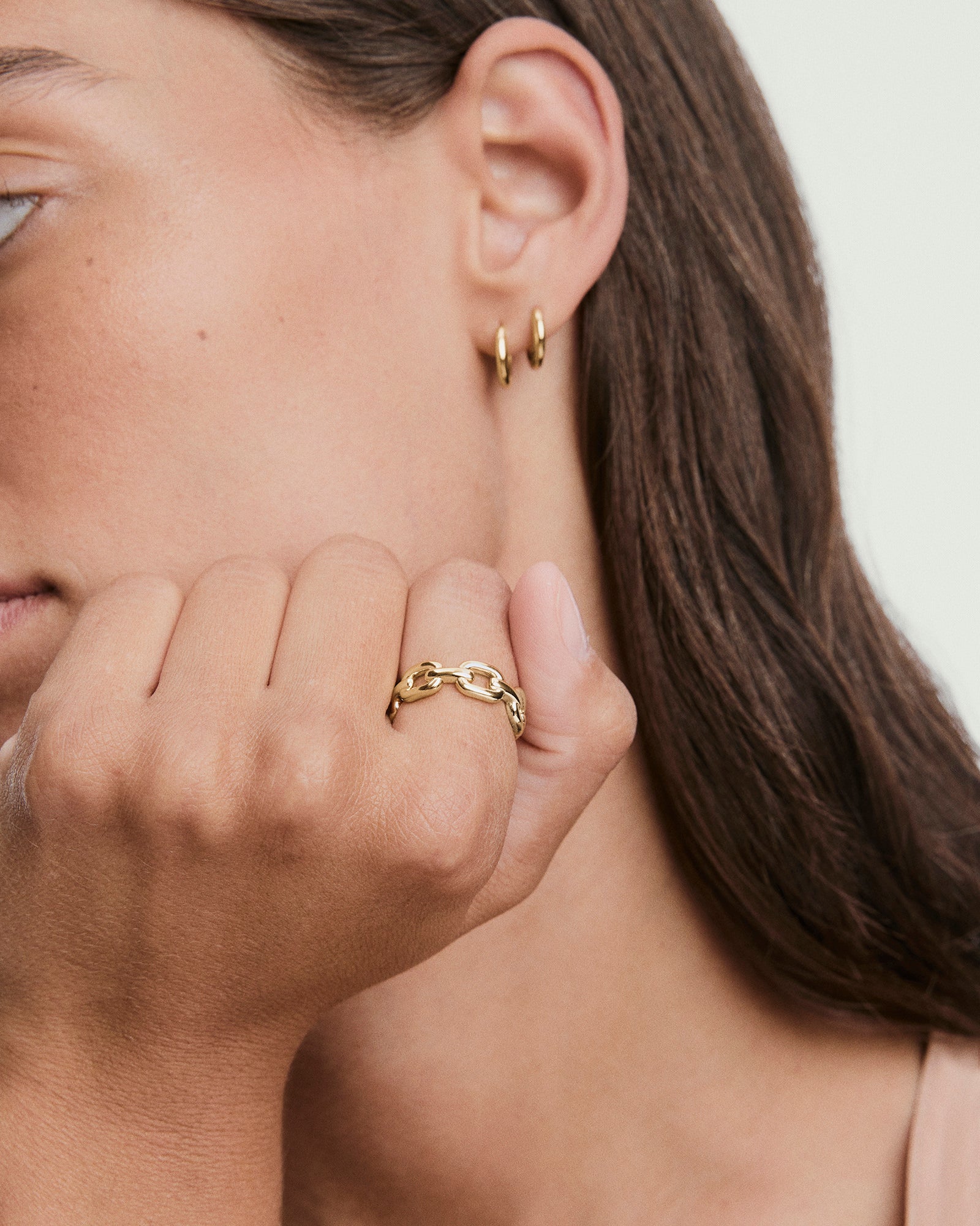Side view of a person with brown hair wearing two gold hoop earrings, showcasing a Stevie Ringâa chunky gold chain-style ring on the index finger.