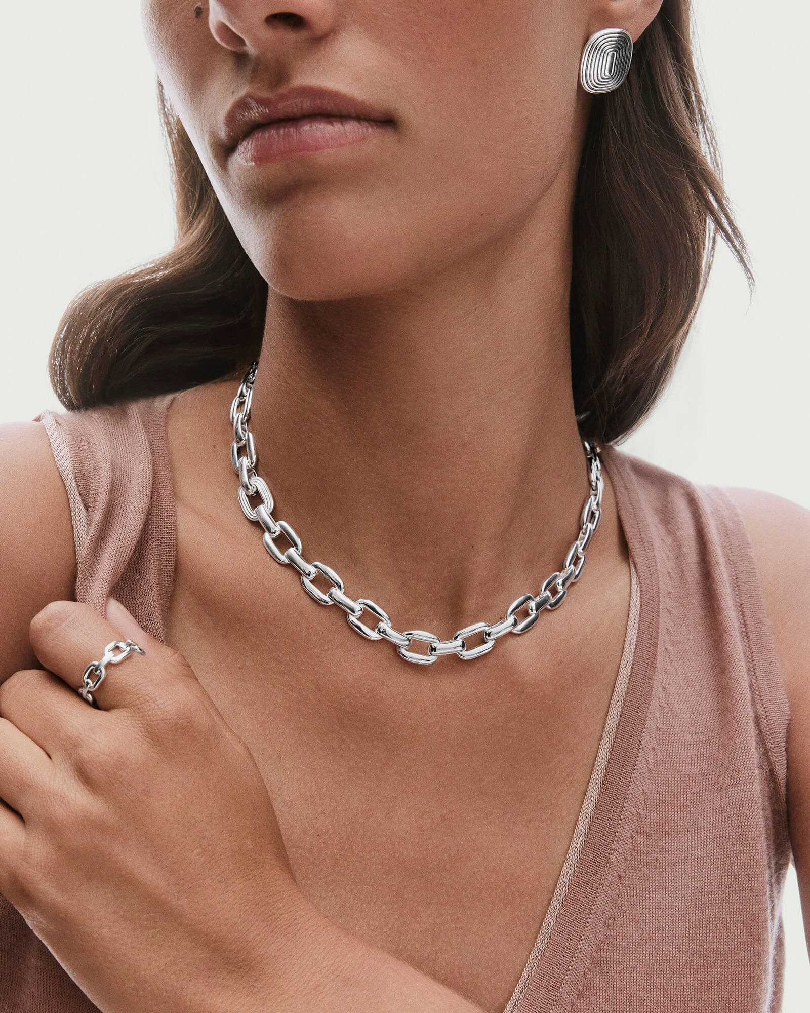 Model wearing Stevie Chain necklace with elongated oval links, paired with a matching silver ring and sculptural earrings, highlighting bold design and shine.