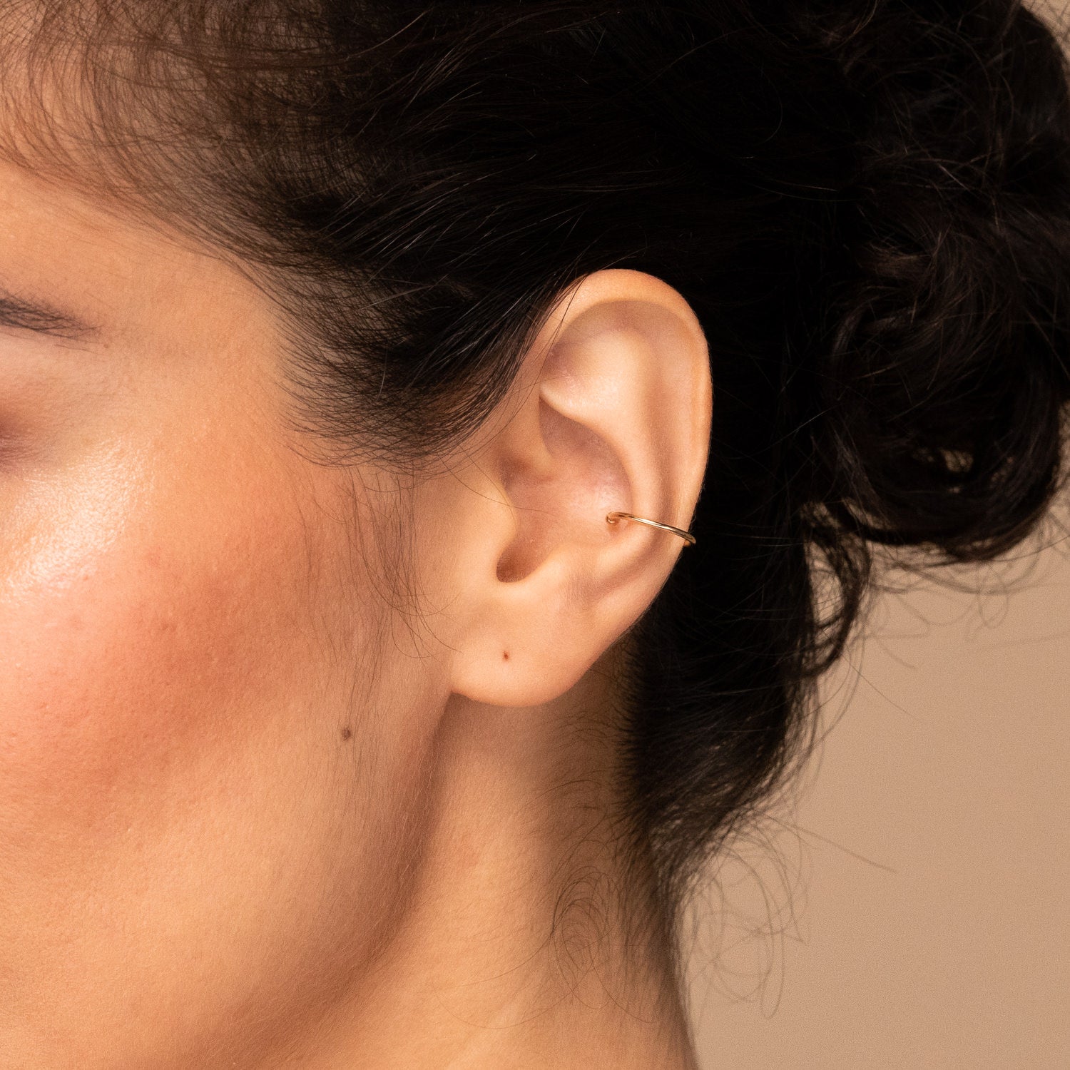 Close-up of a woman's ear wearing the handcrafted 14k gold Essential Cuff ear cuff, enhancing her earring stack.