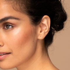 Close-up of a woman's ear wearing the Essential Cuff, a handcrafted 14k solid gold ear cuff, enhancing her earring stack.