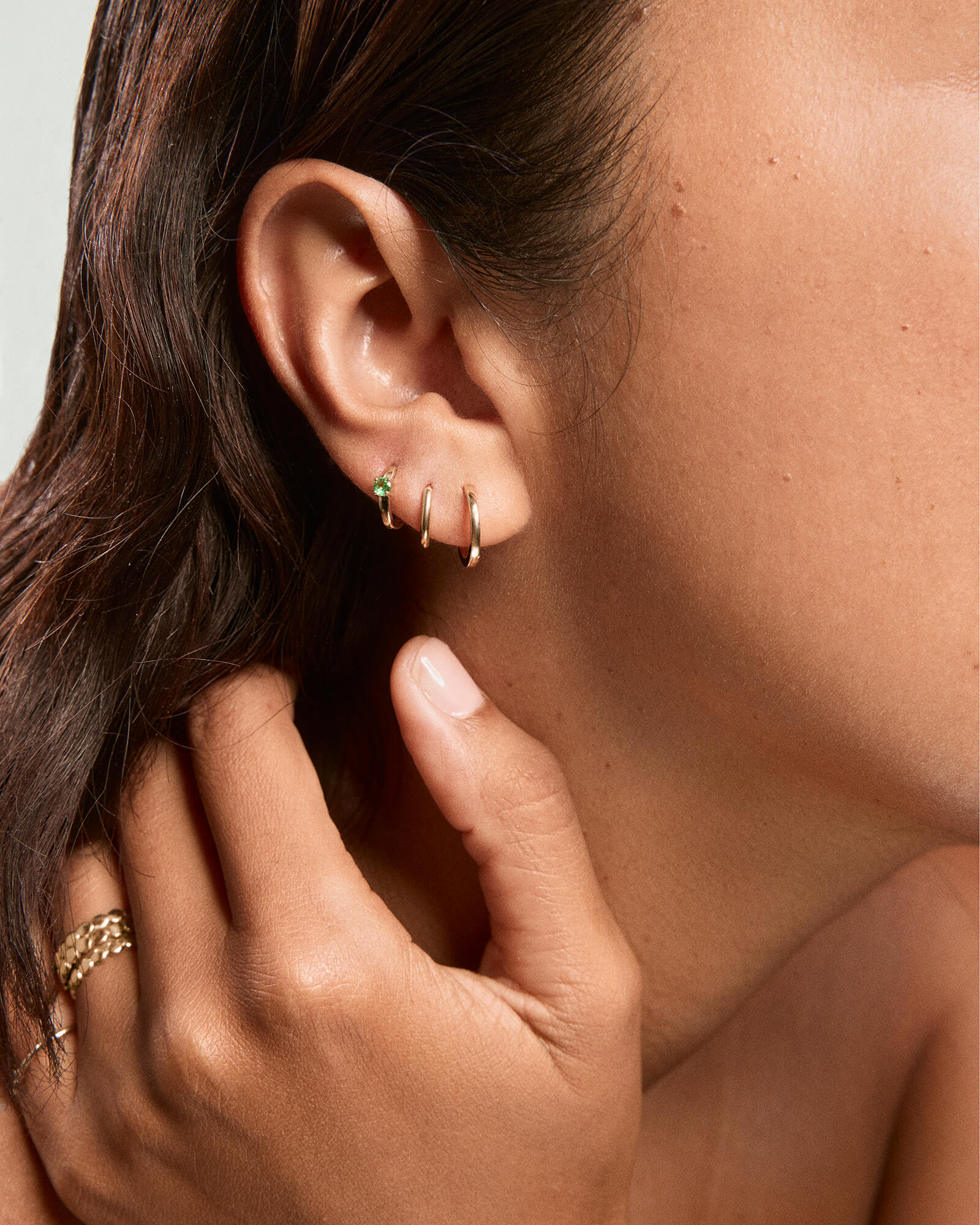 Close-up of a woman's ear wearing a Single Colored Mini Hoop with a hinge clasp, shown alongside other jewelry, highlighting its lightweight, everyday design.