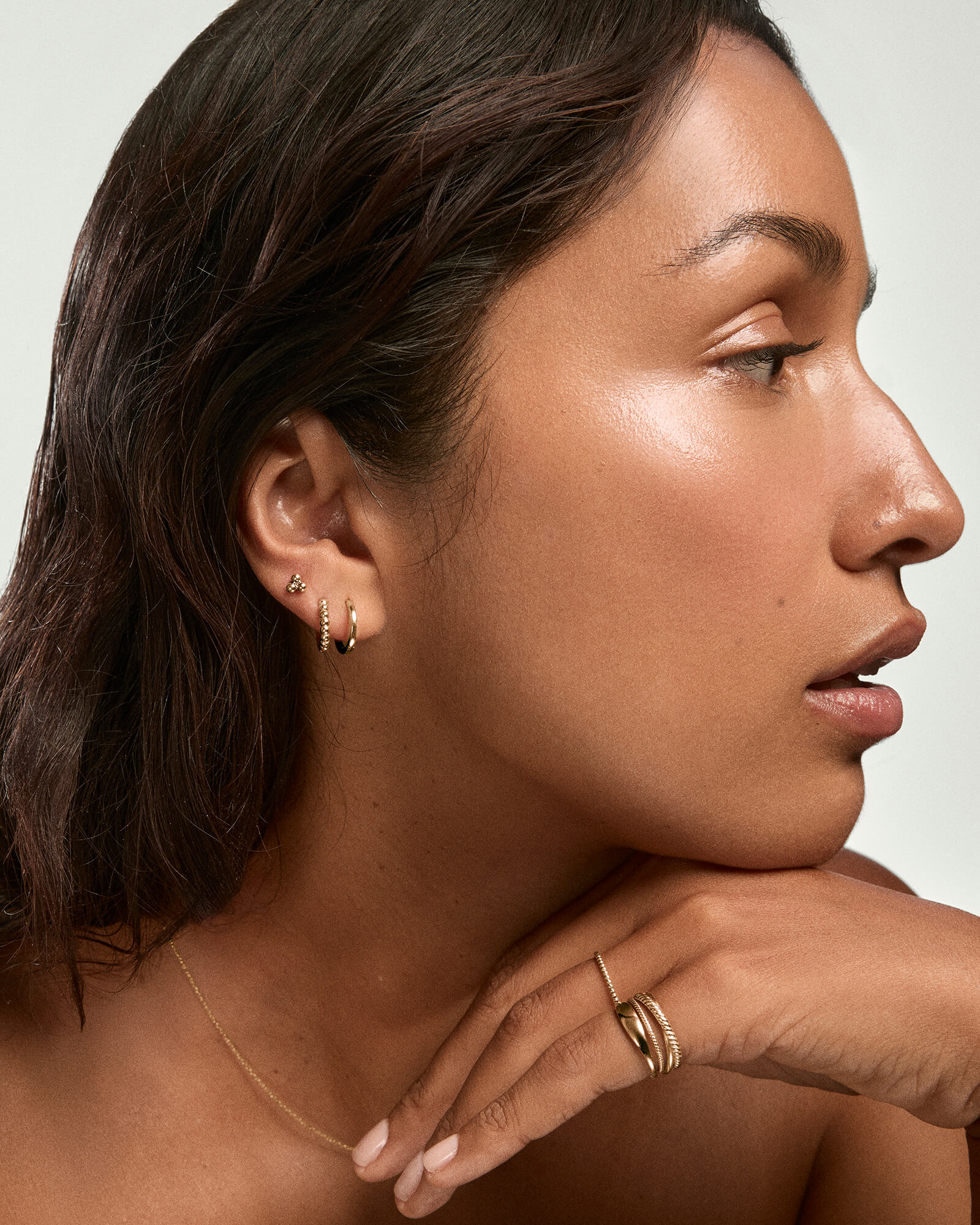 Woman showcasing Spheres Cluster Studs on her right ear, alongside small gold hoops, a delicate chain necklace, and slim rings, highlighting elegant gold jewelry.