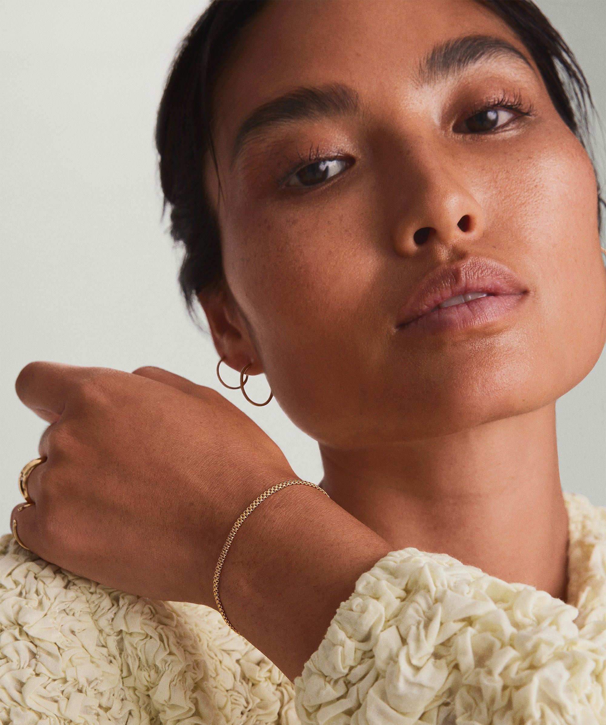 Woman posing, showcasing a sleek, handcrafted 14k yellow gold Timepiece Chain Bracelet on her wrist.