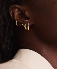 Close-up of a woman's ear wearing a handcrafted 14k solid gold Letter Stud earring, showcasing its elegant initial design.