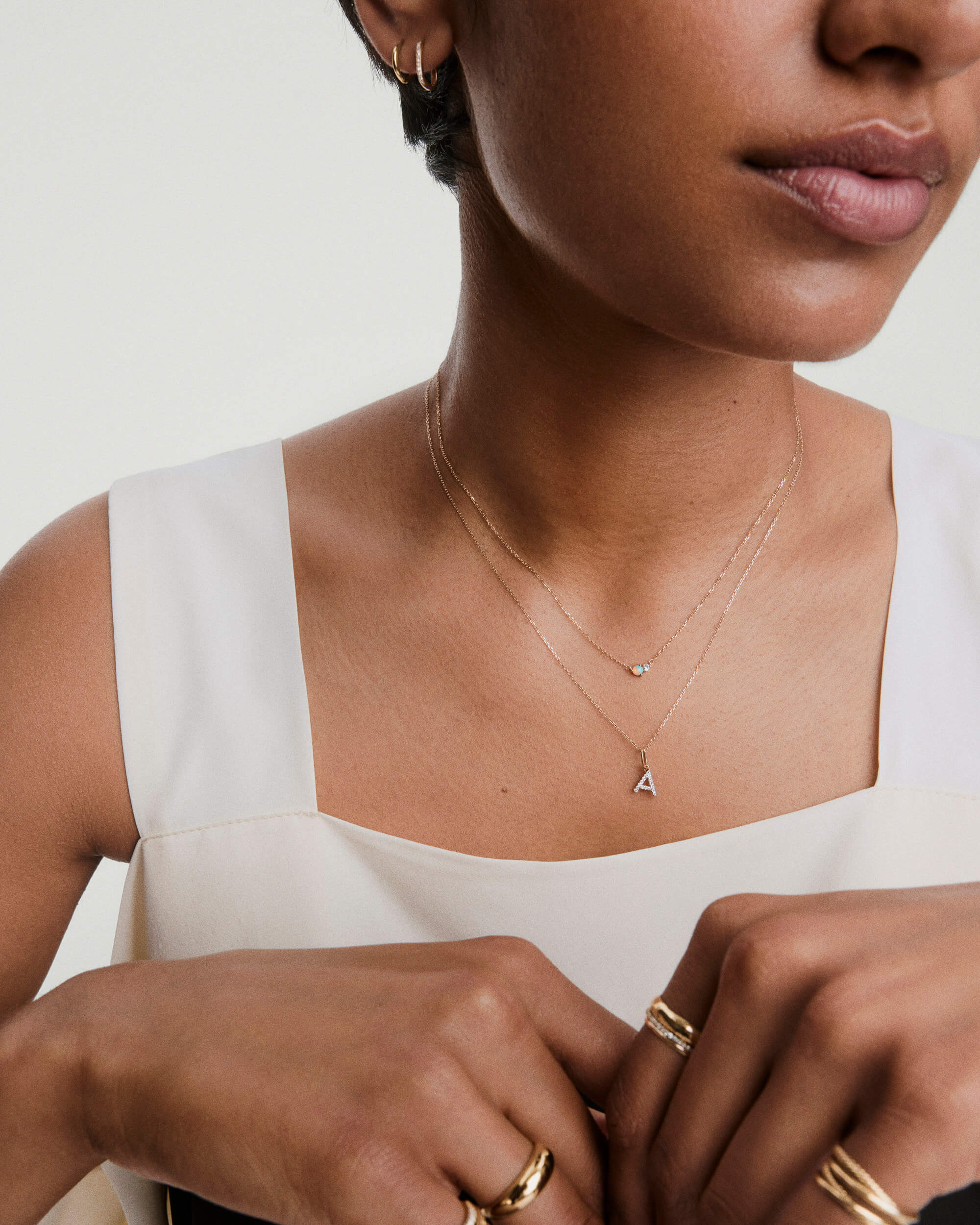 Woman wearing the Beverly Necklace: a delicate gold chain with a trio of tiny opalescent beads and an A initial pendant, paired with minimalist gold jewelry.