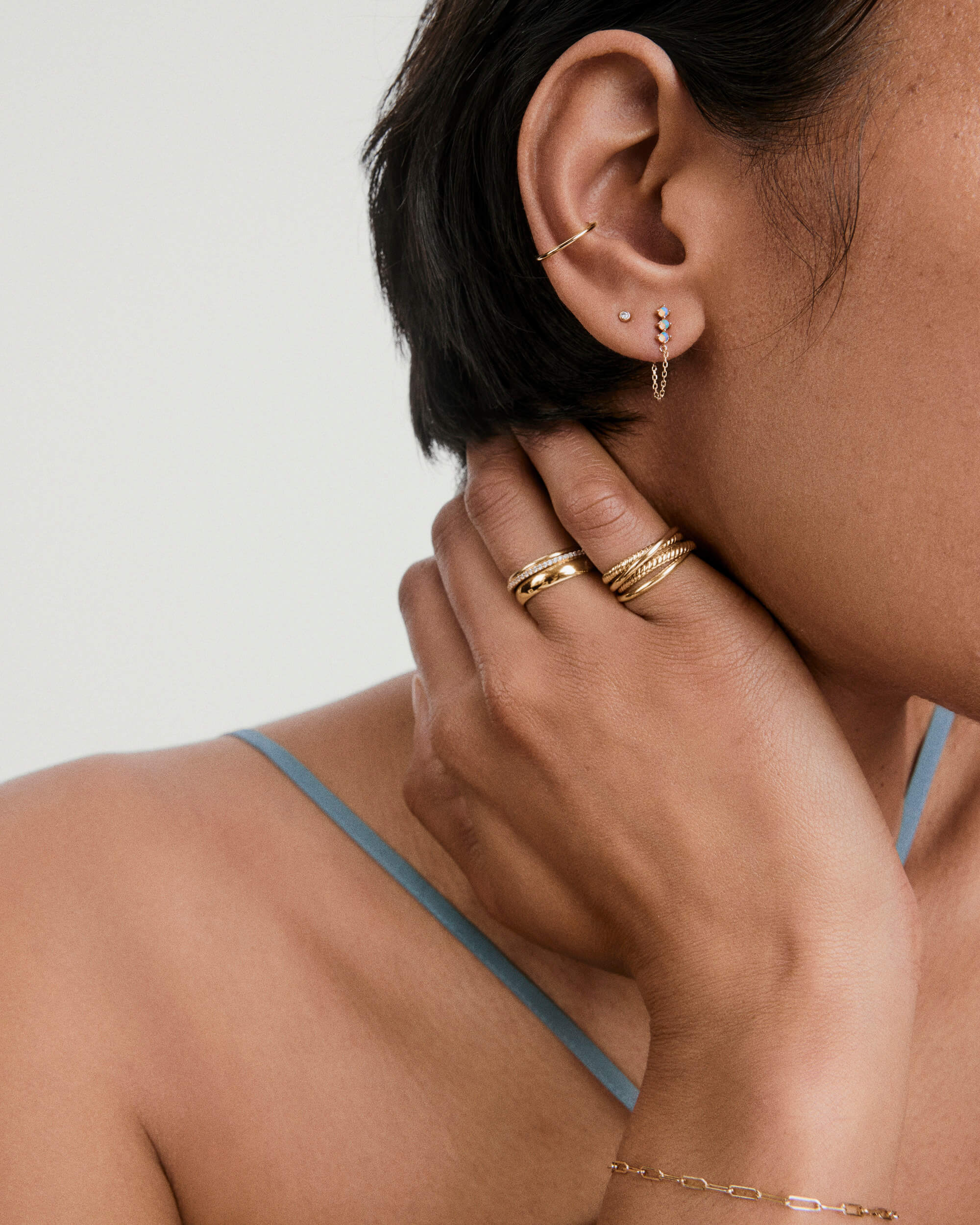 Close-up of ear with Trio Chain Stud featuring opalescent stones and chain tassels, complemented by a gold cuff and stack of rings on the hand.