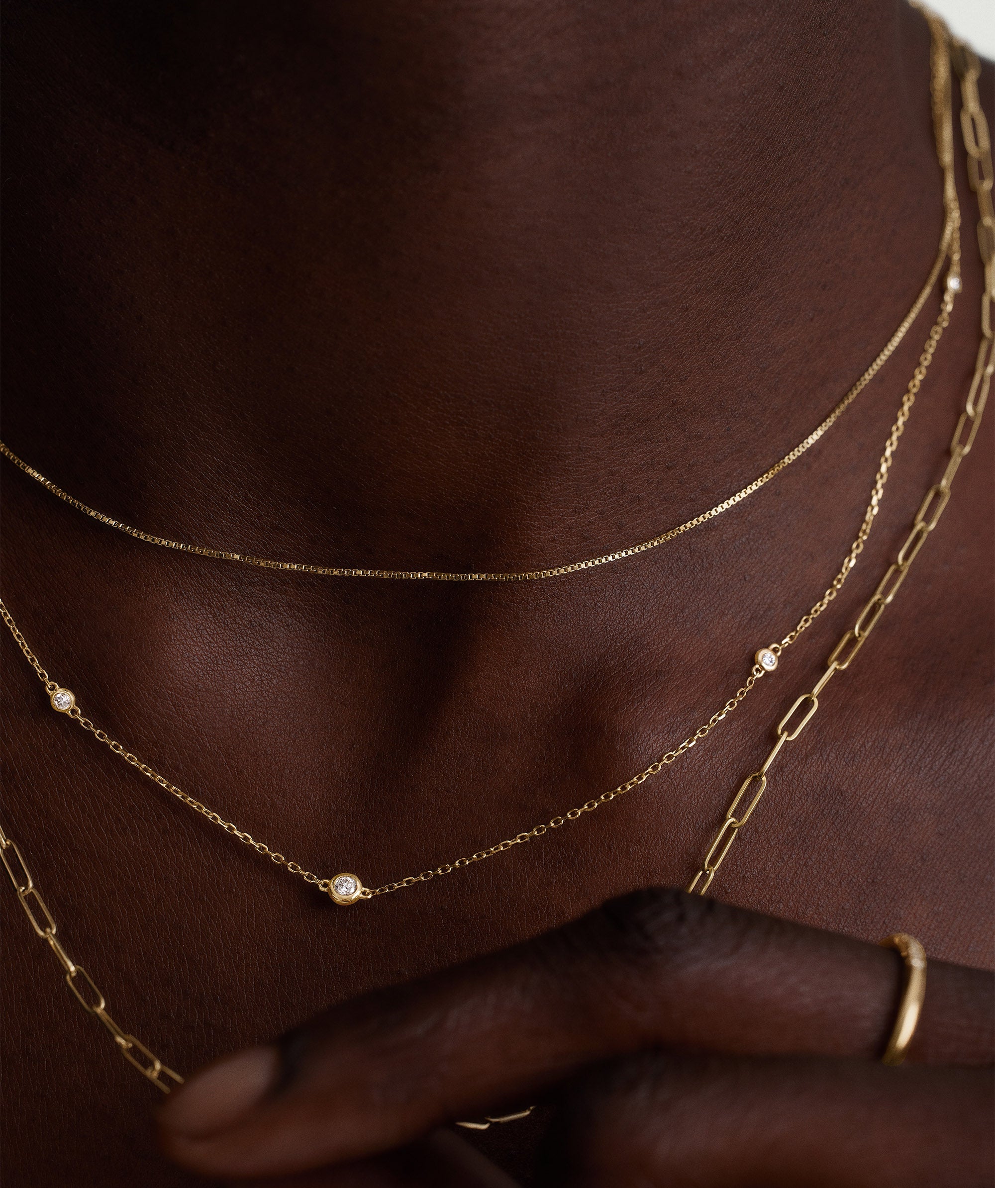 Person wearing the Multi Station Round Diamond Necklace featuring six bezel-set diamonds on a diamond cut cable chain, highlighting its elegant shine and intricate design.