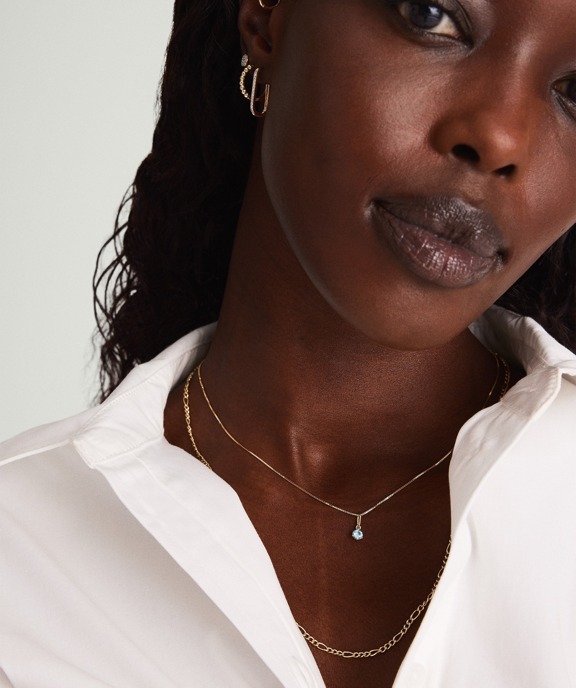 Woman wearing a white shirt and a 14k gold Birthstone Charm necklace, featuring a delicate gemstone pendant.