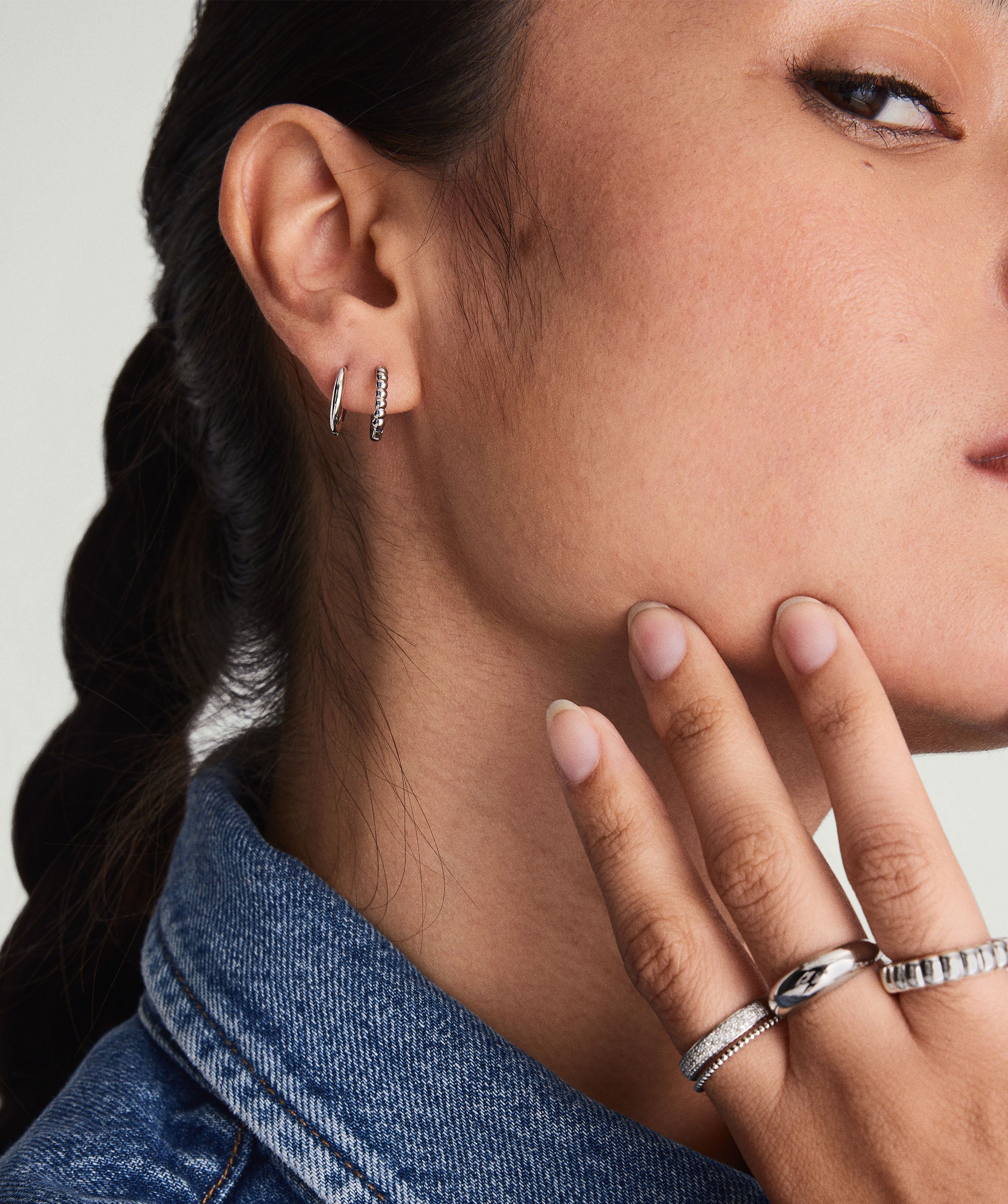 A close-up of a woman wearing Beaded Huggie Hoops, showcasing their intricate design in recycled 14k solid gold. She's touching her cheek, highlighting the earrings.