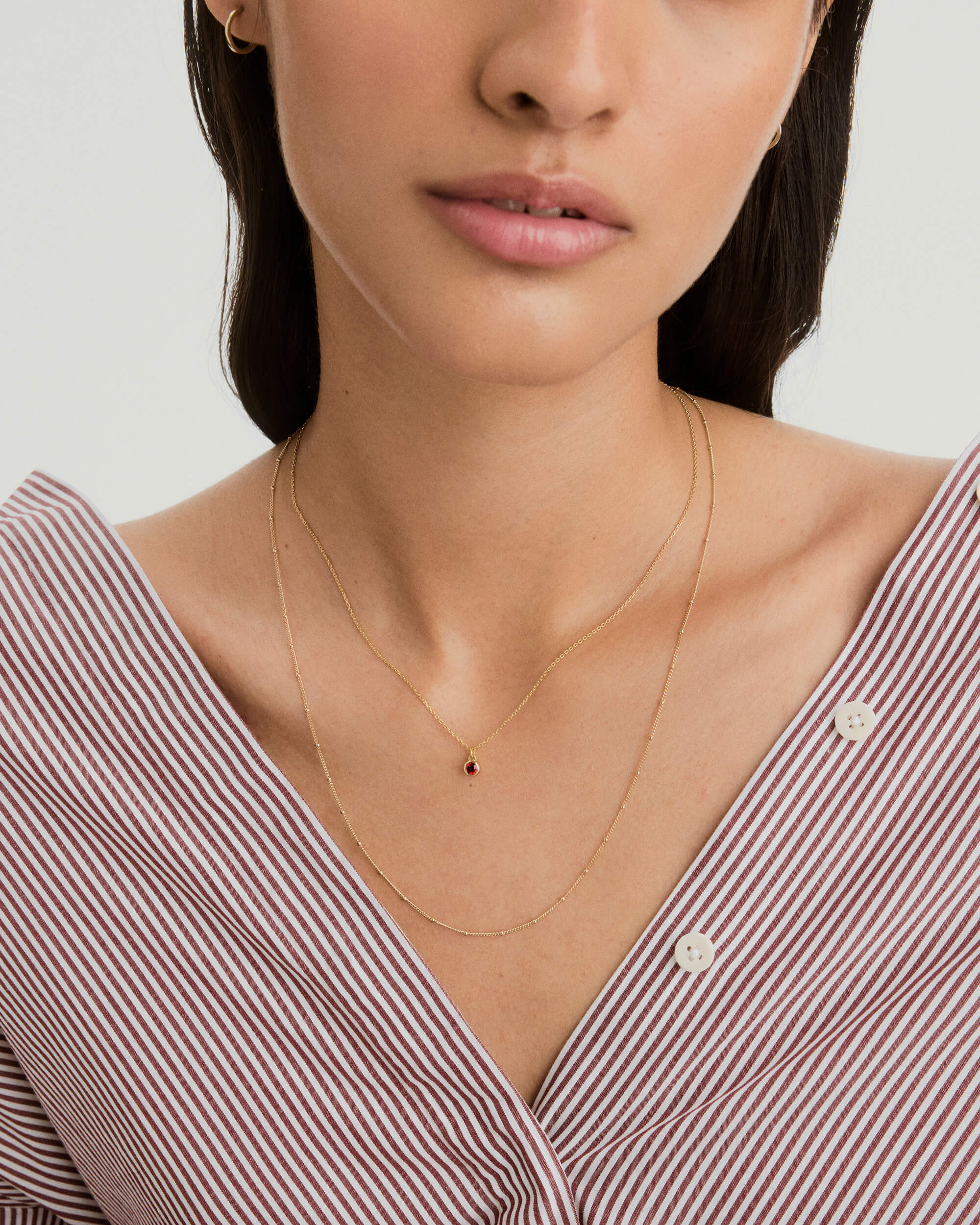 Woman wearing the Sia Birthstone Pendant Necklace, featuring a sparkling gemstone on a chain, perfect for personal or gift occasions.