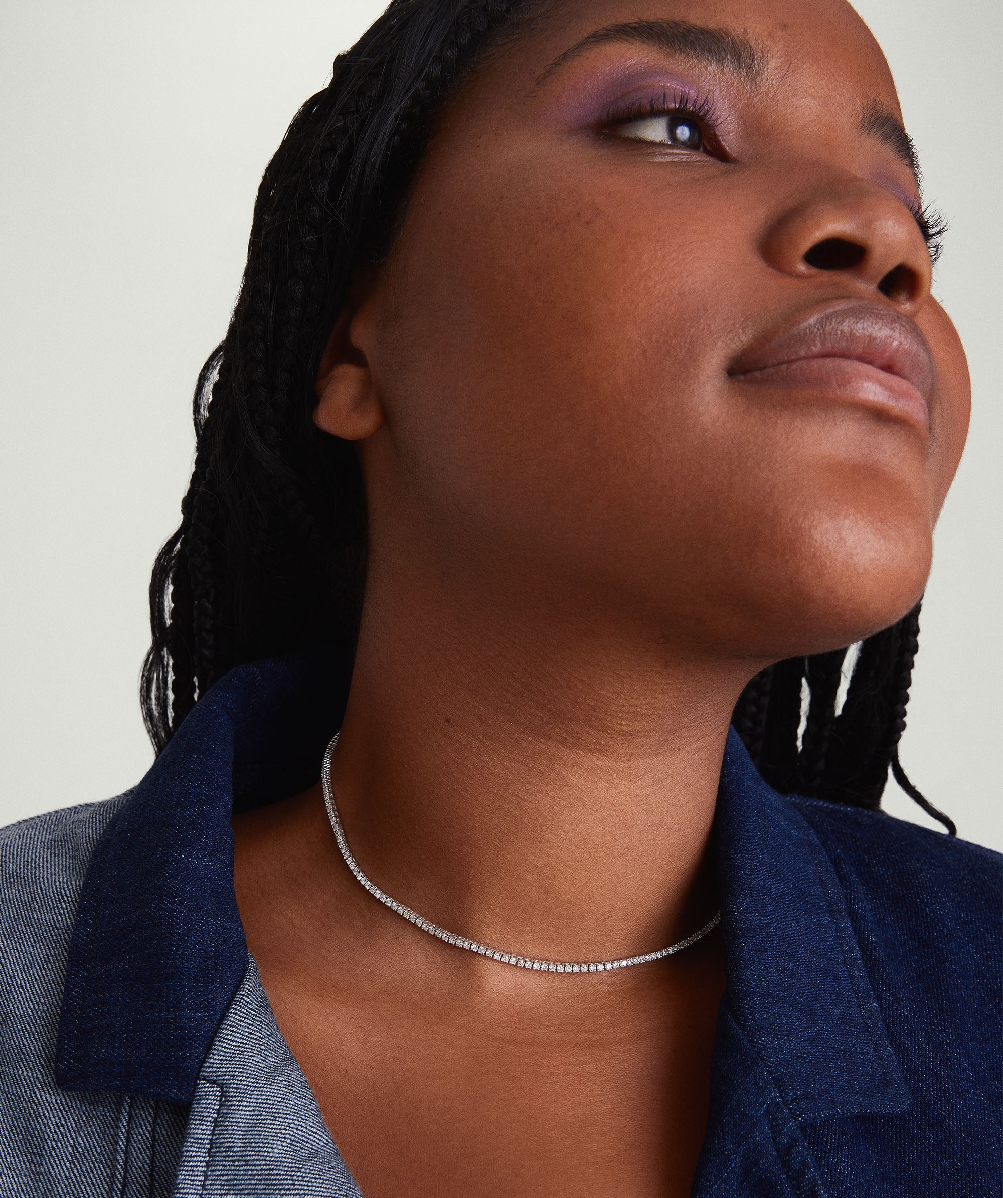 Diamond Tennis Necklace 1.8mm on a woman looking up, showcasing the necklace's sparkle and elegance. The necklace is handcrafted in 14k solid gold with diamonds.