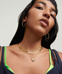 Woman wearing Bold Herringbone Chain Necklace, styled with gold hoop earrings, showcasing the necklace's elegant design and layering versatility.