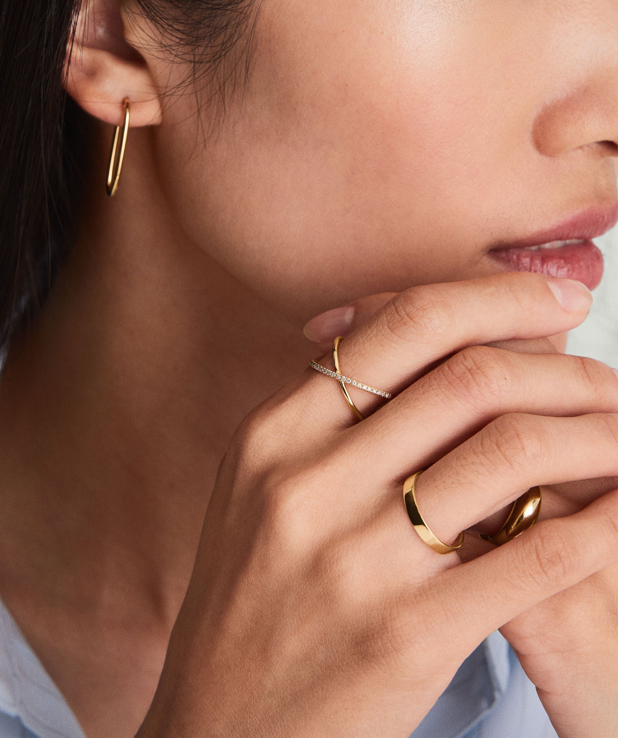 Close-up of a hand wearing the Bold Stacker ring, featuring a plain band and an X-style design with sparkling stones, paired with a gold hoop earring.