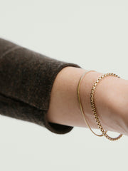Person wearing a brown sweater showcases the Cobra Bracelet, a gold chain accessory elegantly draped around the wrist, highlighting its intricate design.