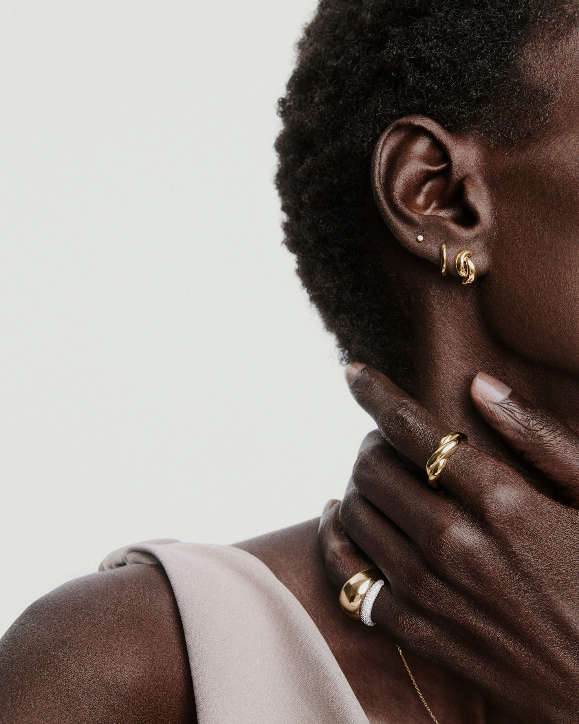 Individual displaying jewelry with focus on Brioche Ring: a smooth, sculptural gold band on the hand, highlighted among other elegant accessories.