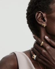 Individual displaying jewelry with focus on Brioche Ring: a smooth, sculptural gold band on the hand, highlighted among other elegant accessories.