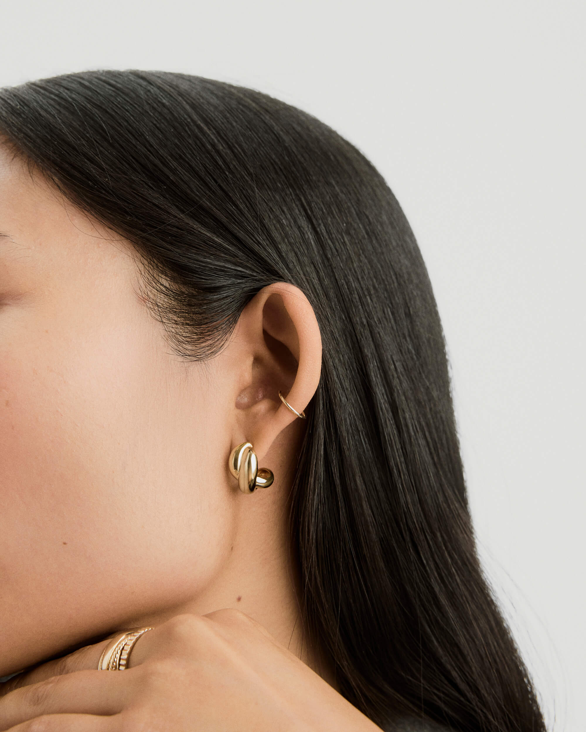 Close-up of a woman's ear wearing Brioche Hoops, gold earrings with a knot design, perfect as an everyday fashion accessory.